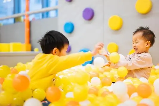 Two children playing together in the yellow and orange ball pit at MosKiddo
